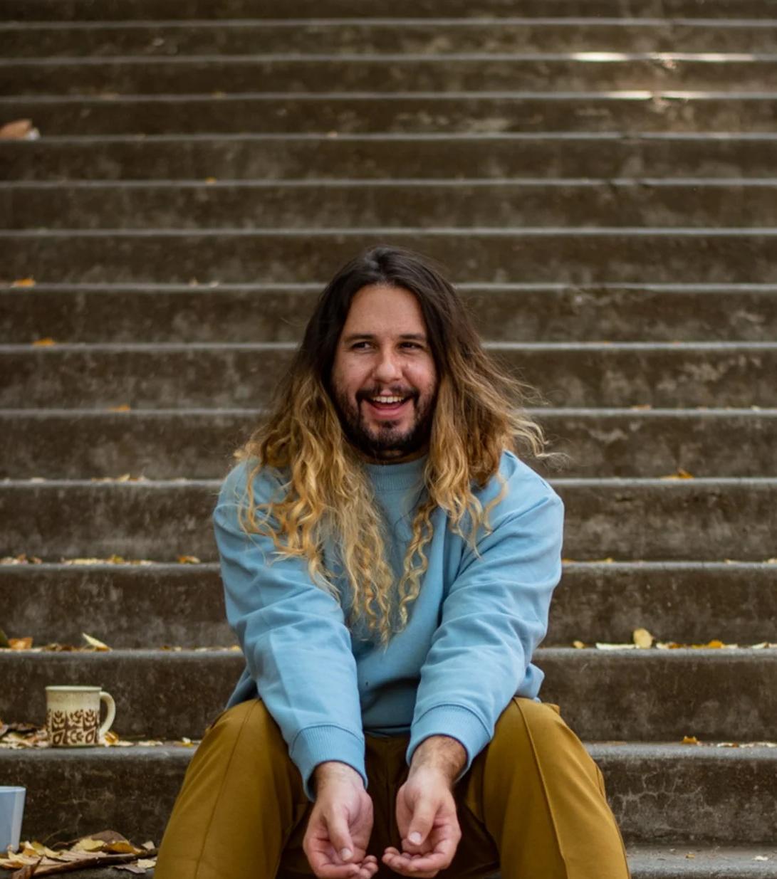 Andrew Merrell sitting at the bottom of stairs, smiling and looking to the right